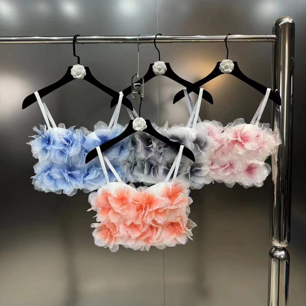 Four women's floral appliqué crop tops in blue, gray, pink, and peach hanging on black hangers on a metal rack