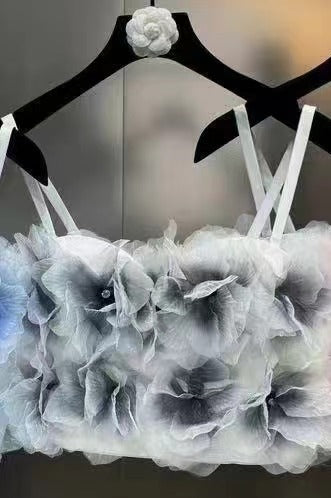 Delicate gray floral crop top with layered fabric flowers hanging on black hangers against a neutral background