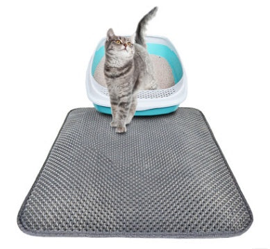 Grey tabby cat walking on a black honeycomb cat litter mat in front of a blue and white litter box