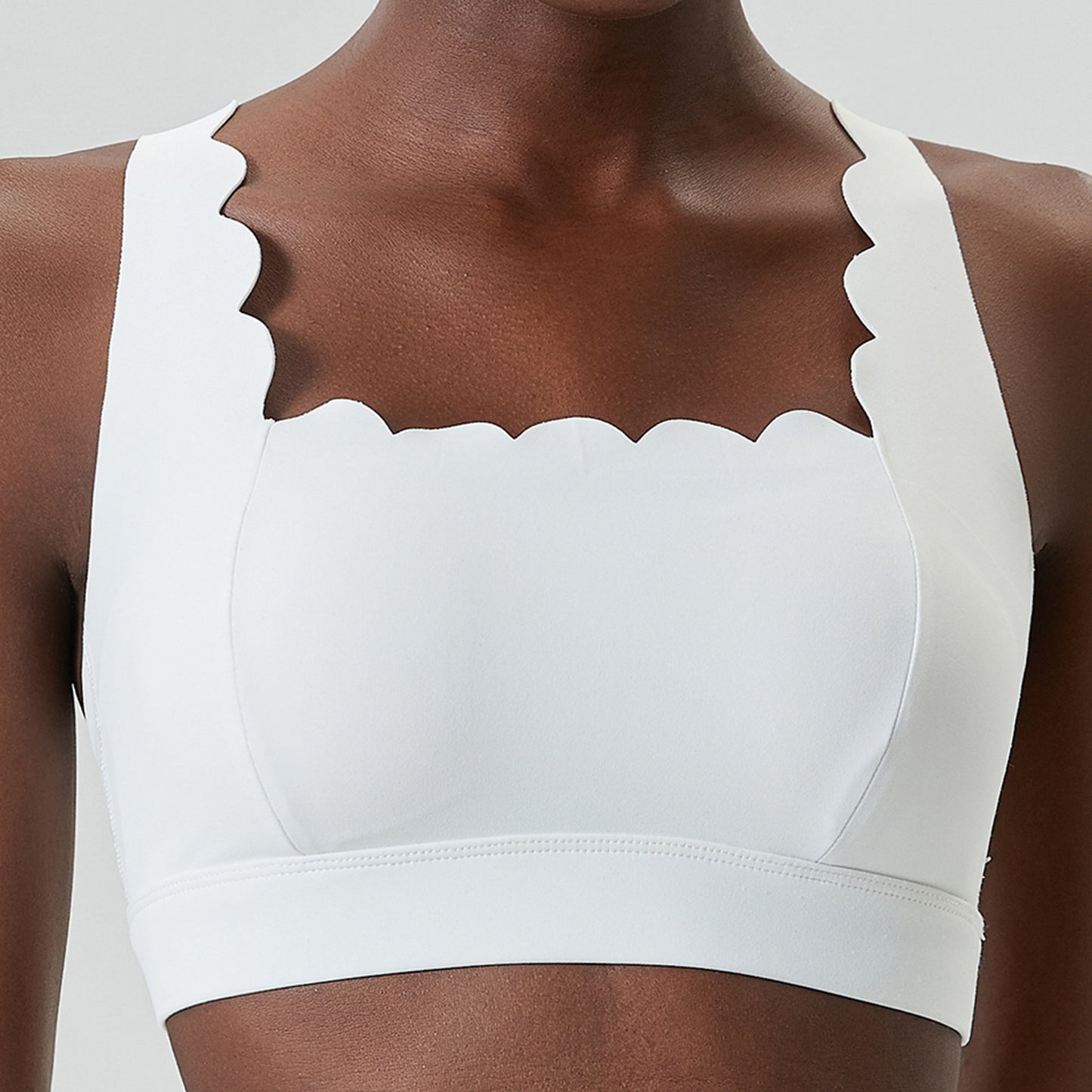 Close-up of a woman wearing a white sports bra with scalloped edges and wide straps