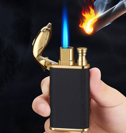 Hand holding black and gold metal double flame lighter with fish-shaped cap lighting a cigar