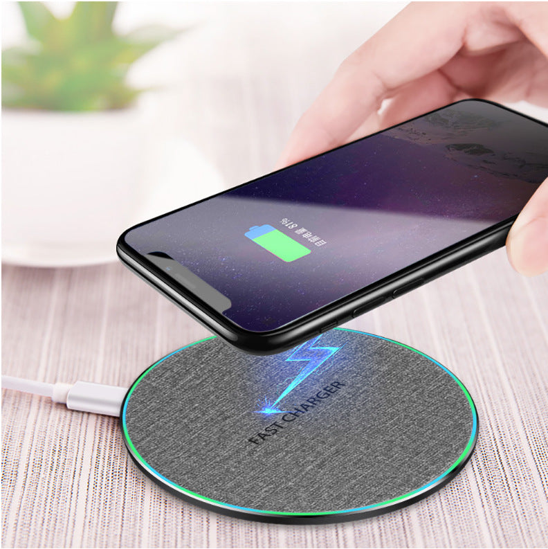 Hand holding smartphone wirelessly charging on gray fabric fast wireless charger pad with blue lightning symbol