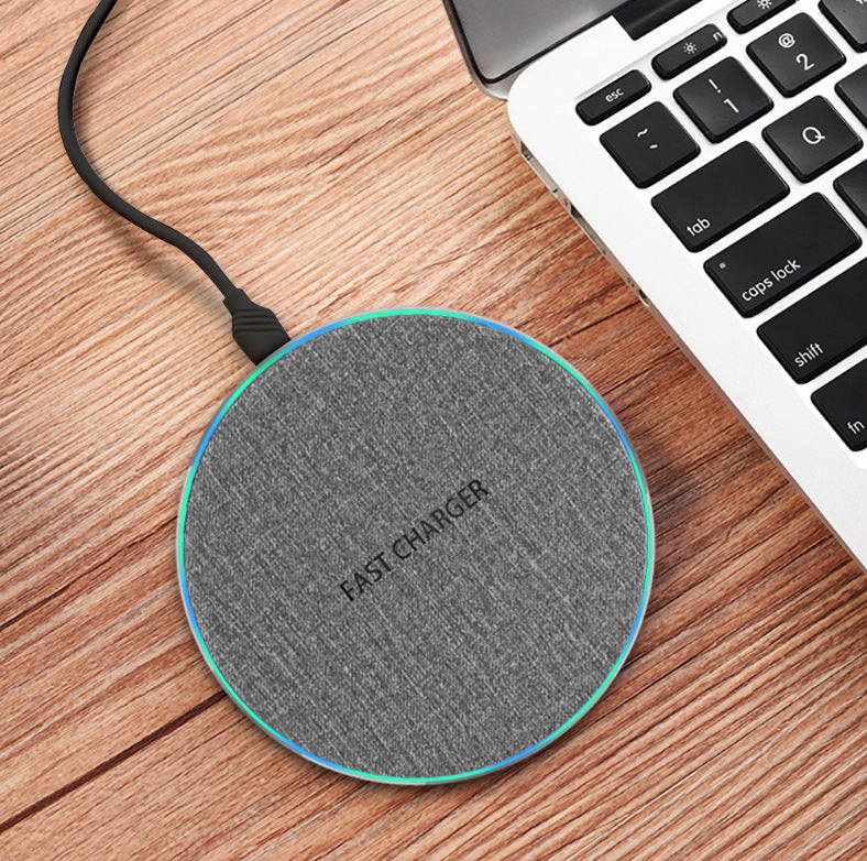 Gray fabric fast charger wireless charging pad connected on wooden desk near laptop keyboard
