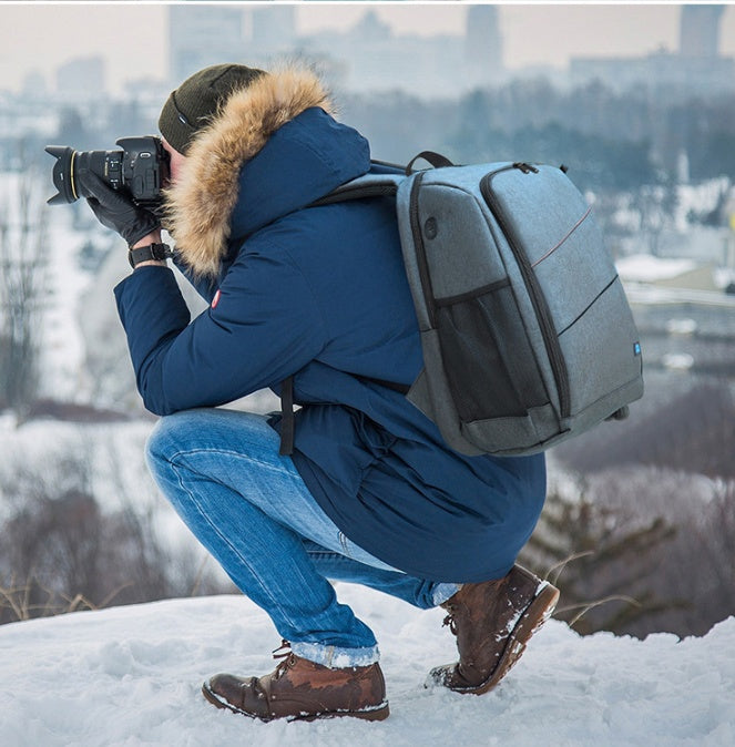 Photographer in winter wear with a waterproof grey camera backpack taking photos in snowy outdoor setting