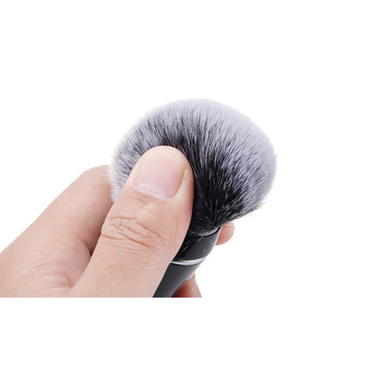 Close-up of hand holding soft black and white makeup brush with dense bristles on white background