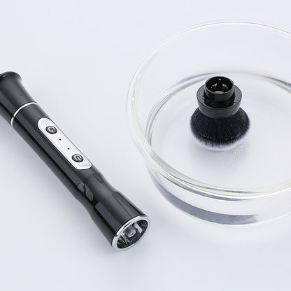 Black electric makeup brush handle with USB charging and detachable soft bristle head in clear bowl