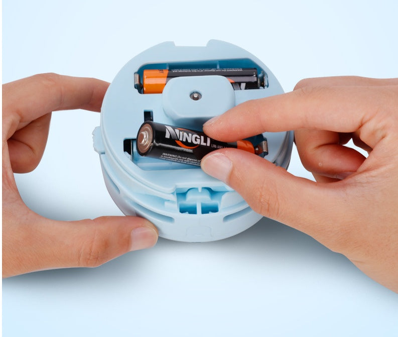 Hand inserting AA battery into blue mini electric desktop vacuum cleaner battery compartment