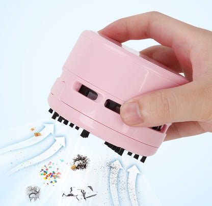 Hand holding a pink mini electric vacuum cleaner picking up small debris on a white surface