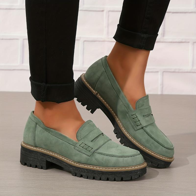 Women's green suede loafers with thick black lug soles worn with black rolled-up pants