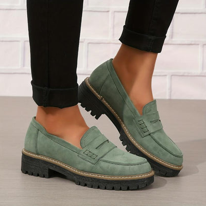 Women's green suede loafers with thick black lug soles worn with black rolled-up pants