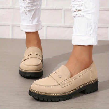 Beige women's loafers with thick black sole worn with white ripped jeans on gray floor