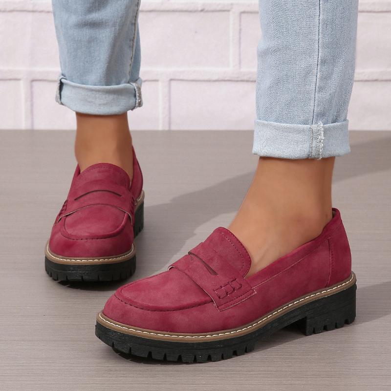 Women wearing thick-soled burgundy suede loafers with stitched details and black treads, paired with cuffed light blue jeans