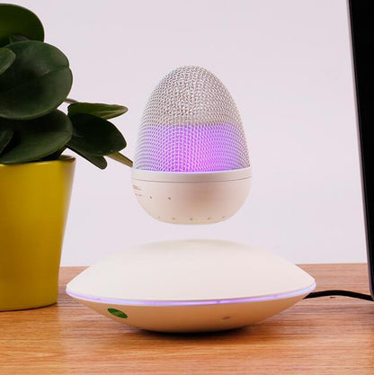 White magnetic levitation wireless Bluetooth speaker floating above its base with purple light on wooden surface