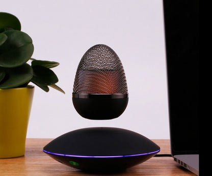 Black egg-shaped levitating Bluetooth speaker floating above a round base with purple light on wooden desk