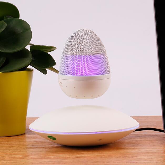 Black levitating Bluetooth speaker with purple light above white base on wooden table