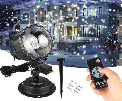 Black LED snowfall projector light with remote control and mounting accessories in front of illuminated house with falling snow effect