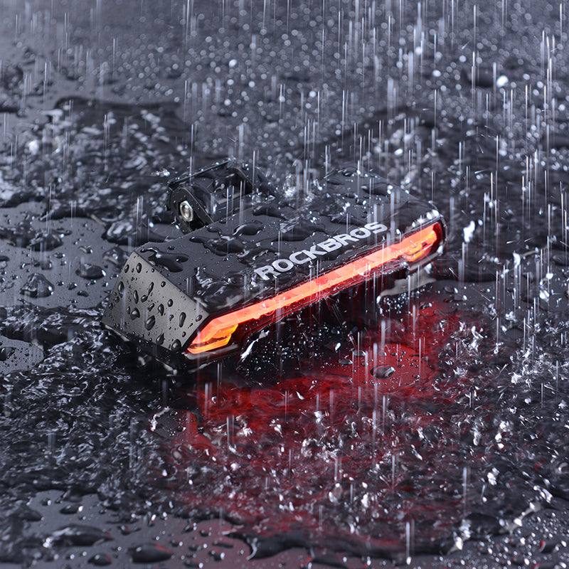 Rockbros black USB rechargeable smart bike tail light glowing red in the rain with water droplets