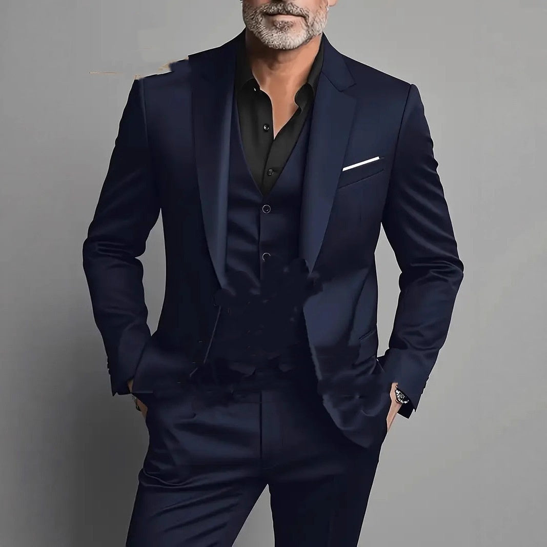 Man wearing a navy blue slim fit three-piece suit with black shirt, pocket square, on gray background