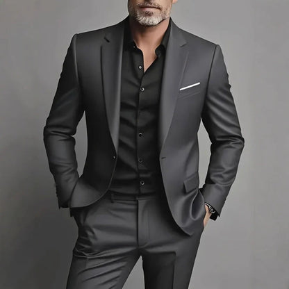 Man wearing black slim fit suit with black shirt and white pocket square on gray background
