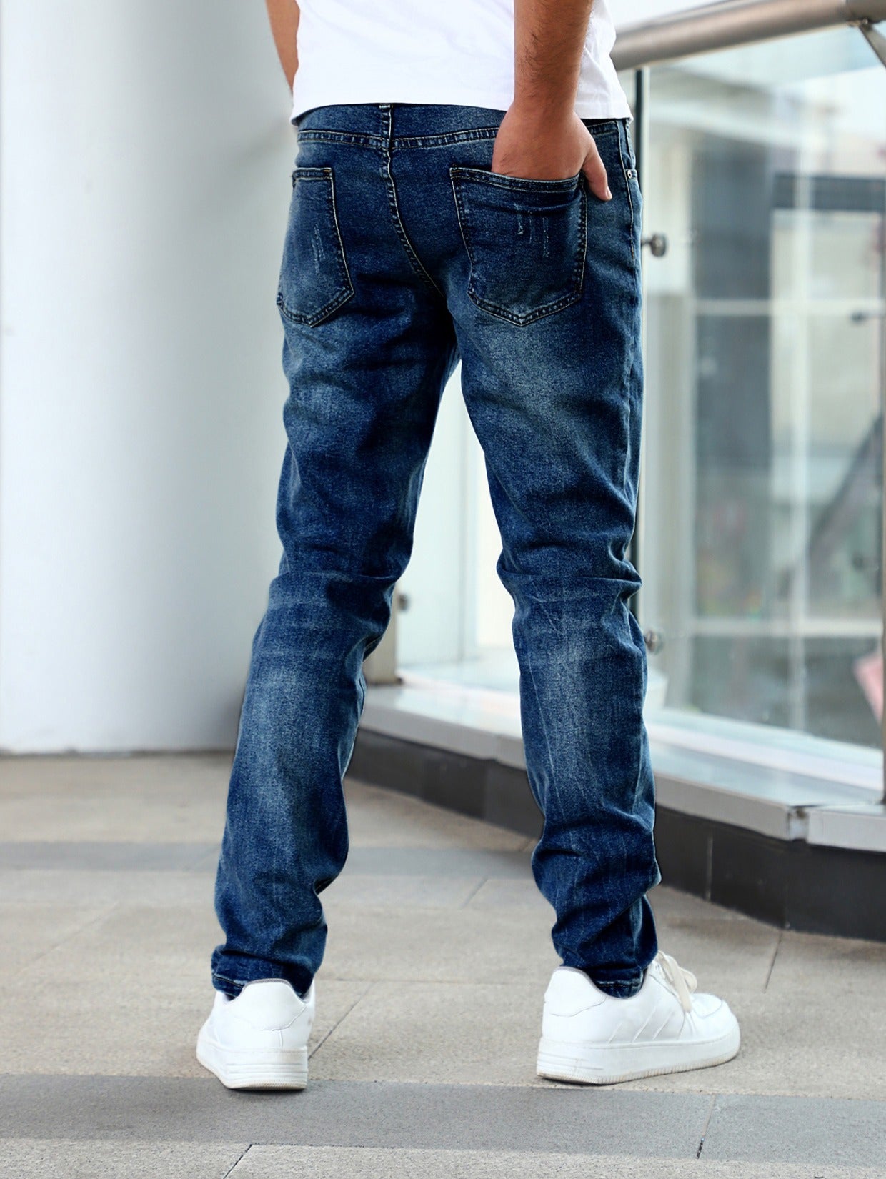 Back view of man wearing slim fit blue denim jeans with mid waist, casual pants and white sneakers