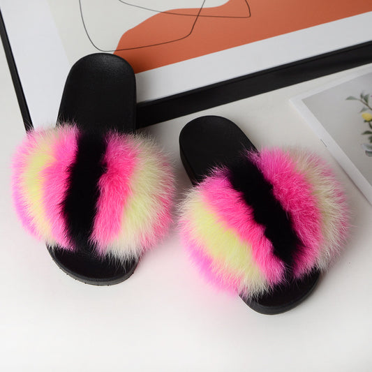 Black slide sandals with vibrant pink, yellow, and black fluffy fur straps on a white surface