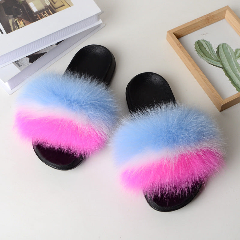 Black slide sandals with blue, white, and pink fox fur straps on white surface with books and cactus frame