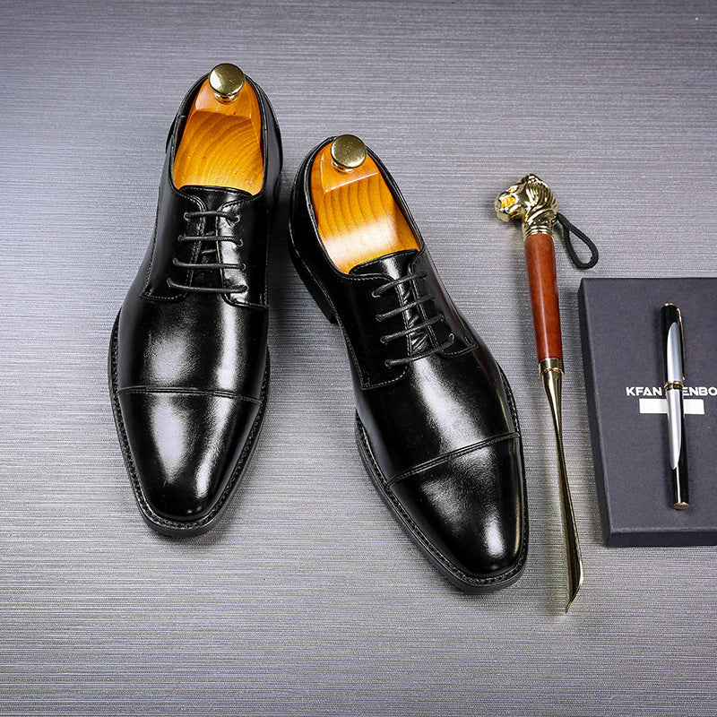 black men's formal leather dress shoes with laces on textured dark surface, alongside tiger-headed shoehorn and black box with pen