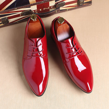 Pair of shiny red men's dress shoes with laces and wooden shoe trees on beige surface