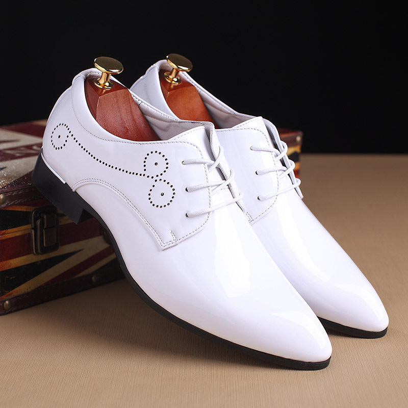 Pair of white glossy men's dress shoes with black sole and decorative perforations, displayed on wooden surface