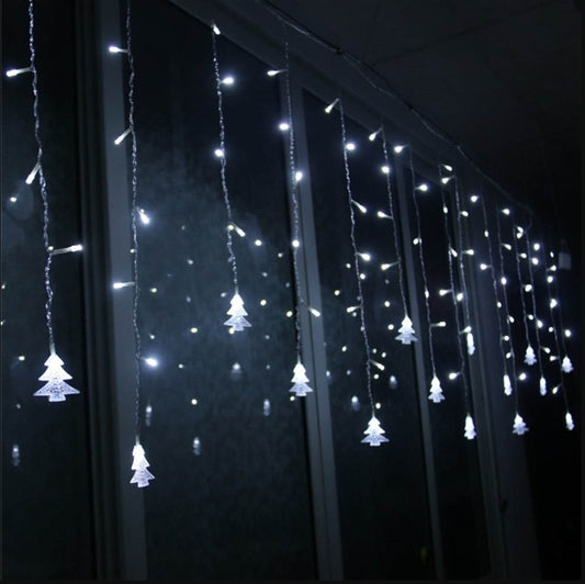 White LED Christmas icicle lights with tree-shaped decorations hanging in front of a window at night