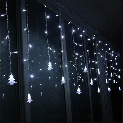 White LED Christmas icicle lights with tree-shaped ornaments hanging in front of a window at night