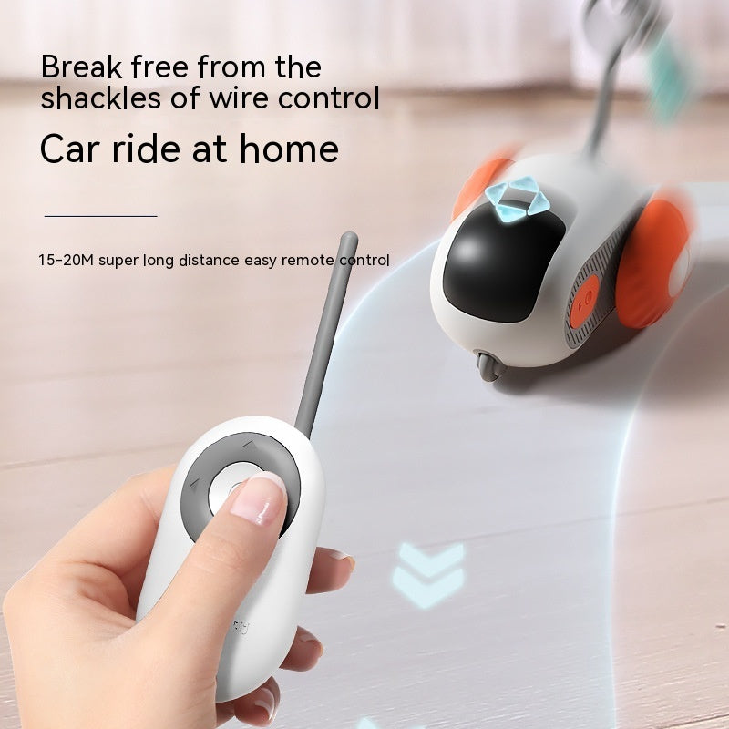 Hand holding white remote control for blue and orange pet interactive car toy on wooden floor