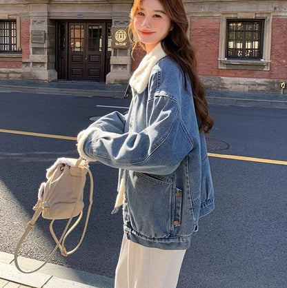 woman wearing blue denim jacket with white fur collar and cuffs, holding beige fur-lined bag on city street