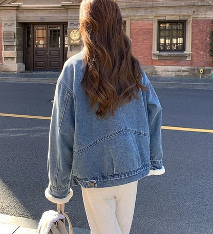 Woman wearing blue denim jacket with white fur cuffs walking on street with building in background