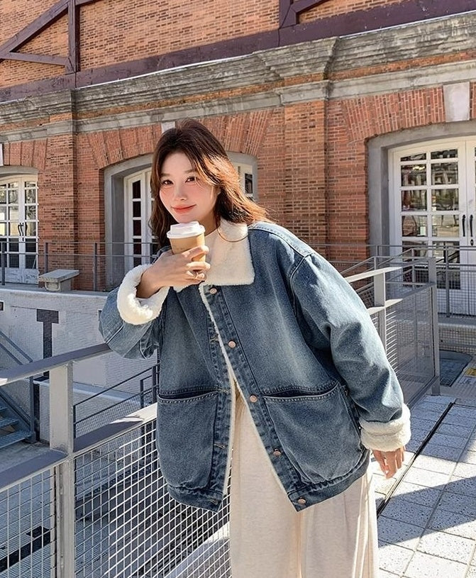 Woman in oversized blue denim jacket with white fur collar and cuffs holding coffee cup outdoors