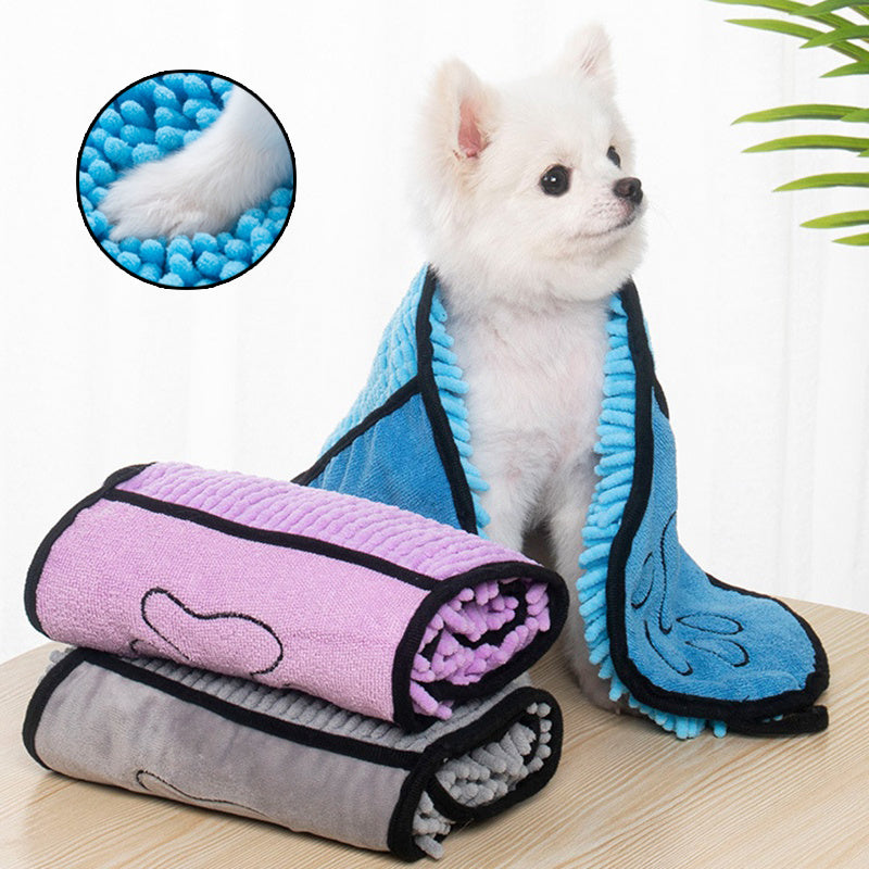 Small white dog wrapped in blue microfiber pet towel with double pockets, next to purple and gray towels on wooden surface