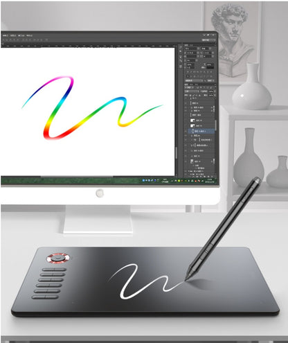 Black graphic drawing tablet with pen on white desk in front of computer screen showing colorful brush stroke