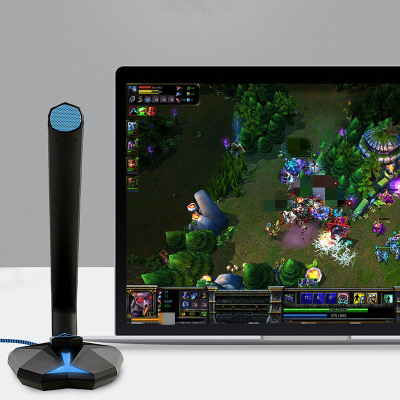 Black omnidirectional USB gaming microphone with blue grille beside laptop displaying online multiplayer game