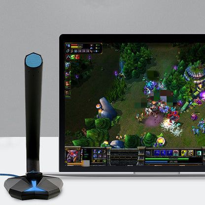 Black omnidirectional USB gaming microphone with blue grille beside laptop displaying online multiplayer game