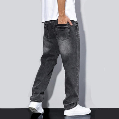 Back view of a person wearing faded black loose-fit straight-leg jeans and white sneakers against a gray background
