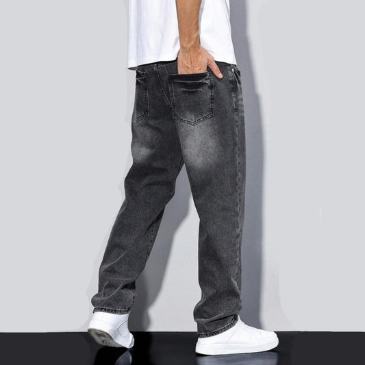 Back view of a person wearing faded black loose-fit straight-leg jeans and white sneakers against a gray background