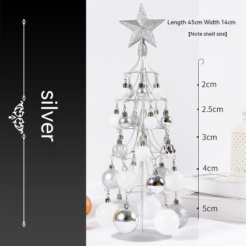 Silver miniature metal Christmas tree with white and silver baubles and glitter star topper on white surface