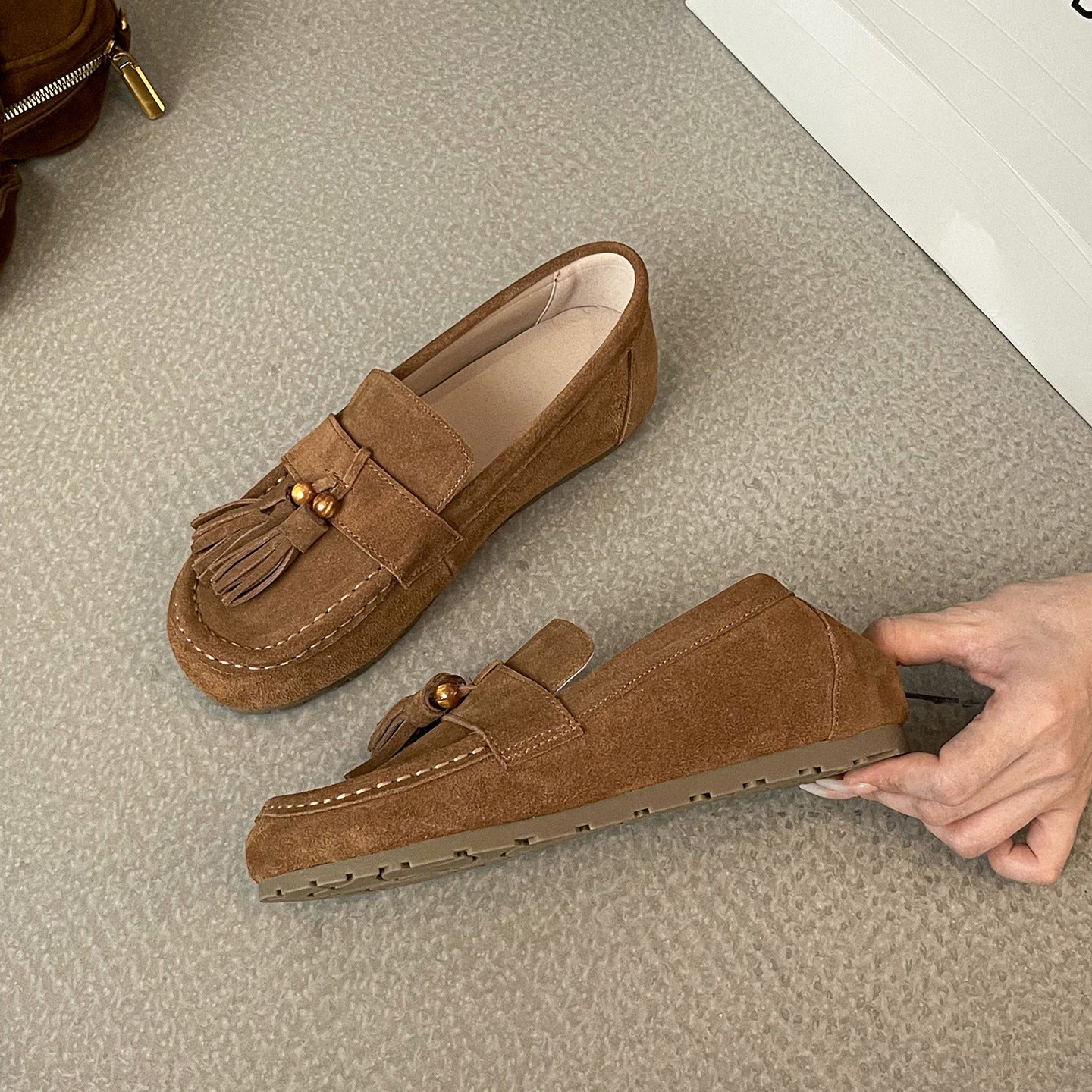 Brown suede women's tassel flat shoes with stitched details on a textured surface