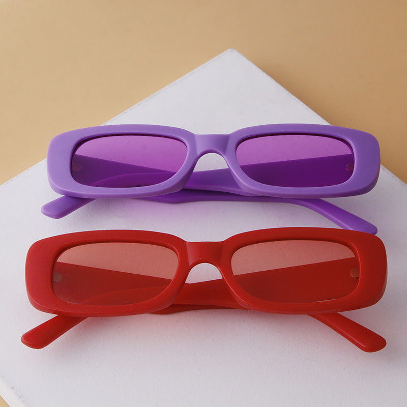 Pair of lightweight rectangular sunglasses with UV protection in purple and red frames on white and beige background