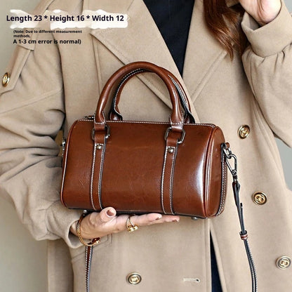 Caramel brown leather crossbody bag with double handles and detachable strap held by person in beige coat