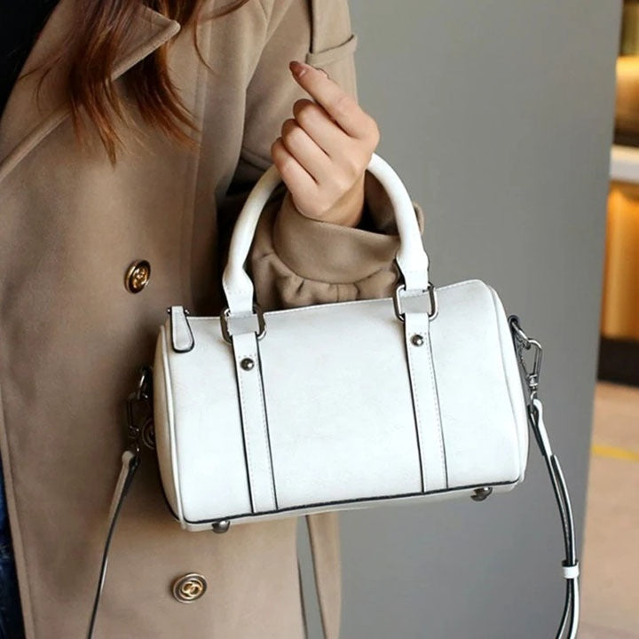Woman in beige coat holding white leather handbag with top handles and shoulder strap