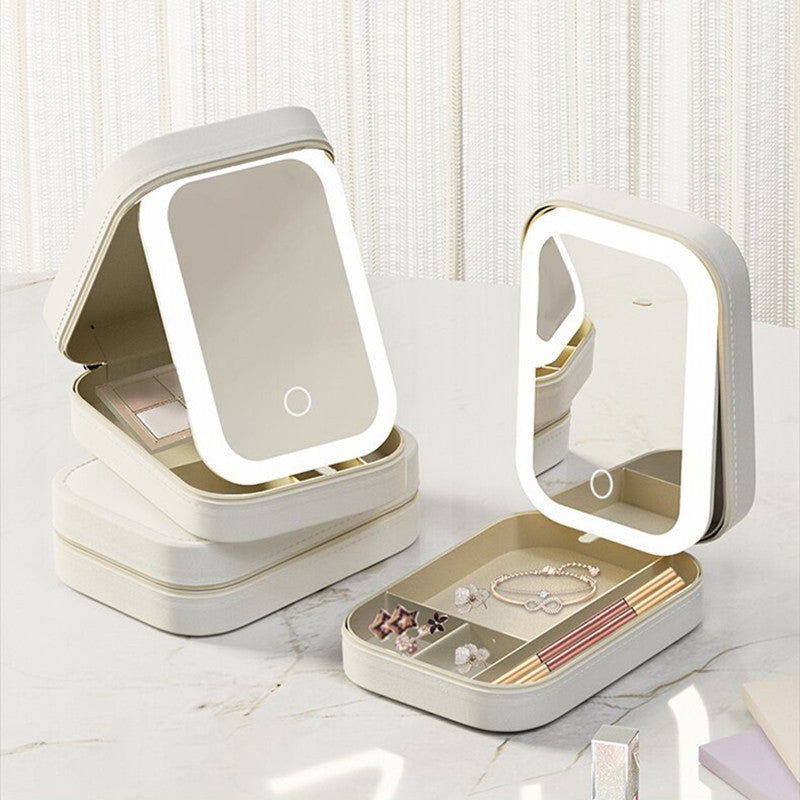 Portable beige vanity case with LED lighted mirror and compartments holding jewelry and makeup items on marble surface