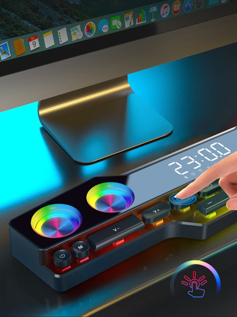RGB Bluetooth speaker shaped like a guitar with volume controls and digital clock display under computer monitor