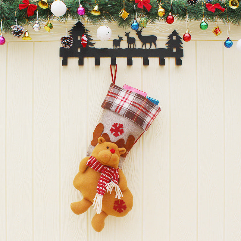 Christmas stocking with plush reindeer and red scarf hanging on black holder under festive garland with colorful ornaments