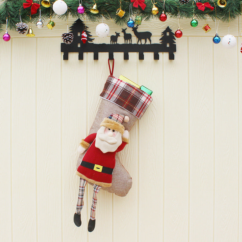 Christmas stocking with plush Santa Claus and gifts hanging under festive garland with ornaments and pinecones